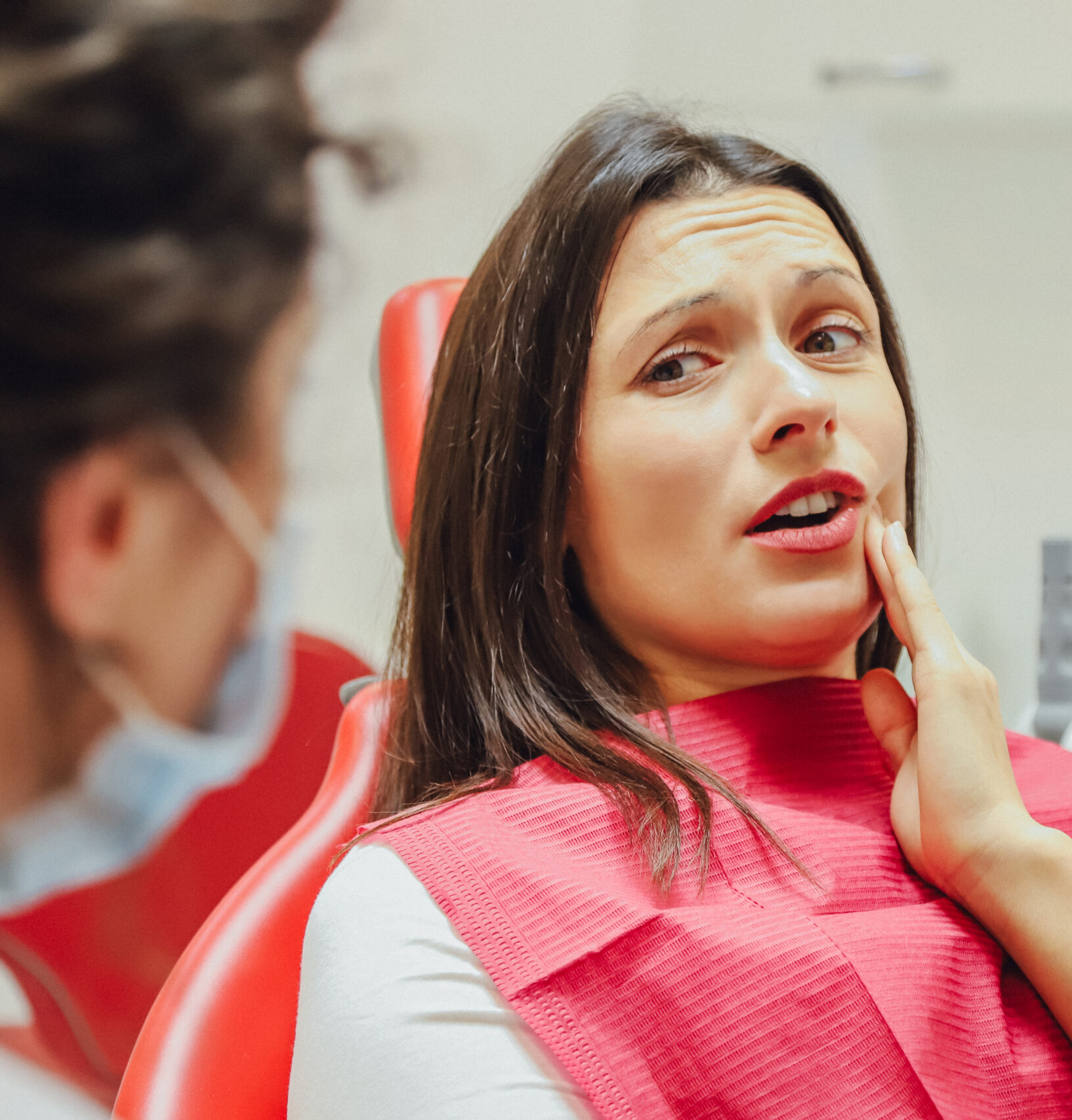 Close-up portrait of a sad young girl with a painful tooth, a doctor in office chairs, an isolated dentist office background clinic. Expressions of the human face, emotions, feelings, reactions
